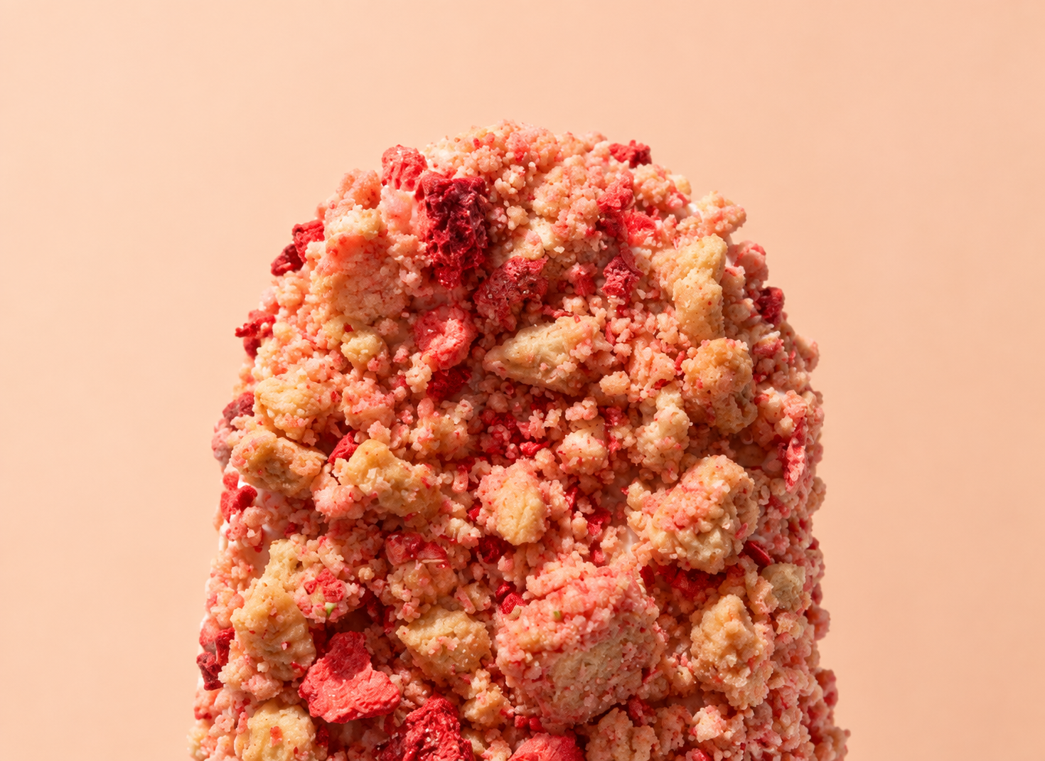 Cakesicle coated in strawberry crunch crumble with freeze-dried strawberry pieces on a peach background